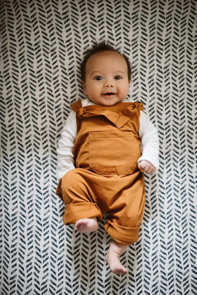 lifestyle portrait of newborn baby smiling in crib