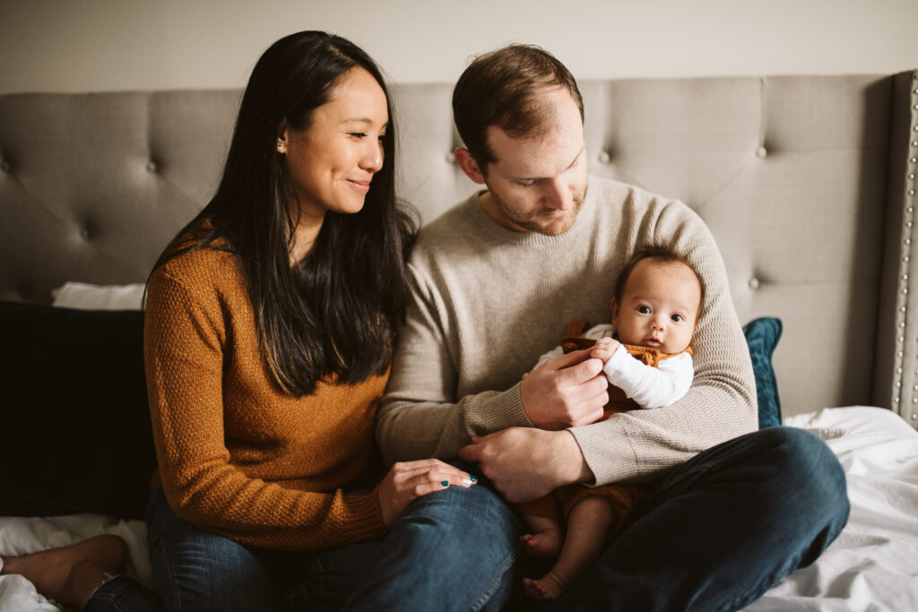 family sitting on bed holding newborn baby