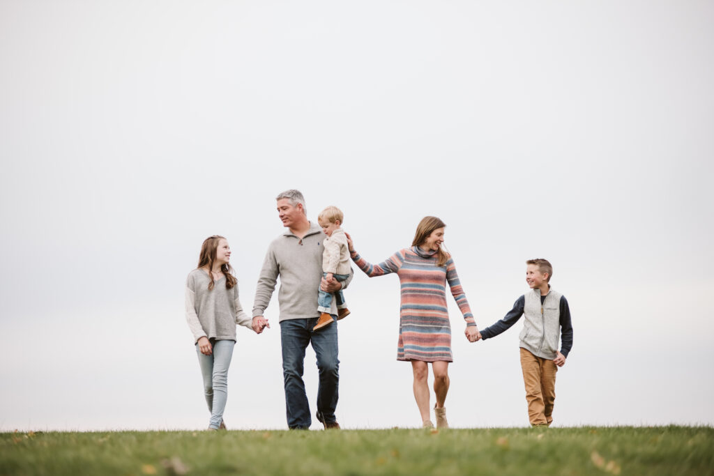 family of 5 holding hands and walking on a field together