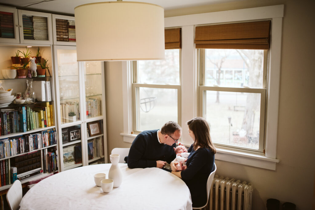 A couple holding their newborn baby in the dinning room. Lifestyle photo by Laura Mares Photography, Pittsburgh Newborn Photographer.