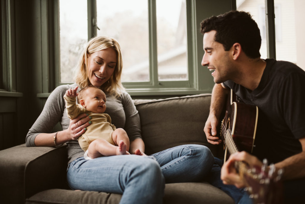 Family sitting on the sofa while the father plays the guitar. Photo by Laura Mares Photography, Pittsburgh Newborn Lifestyle Photographer.