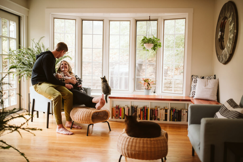 A couple holding their newborn baby with their two cats. Lifestyle photo by Laura Mares Photography, Pittsburgh Newborn Photographer.