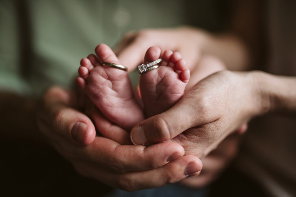 Parents holding their baby's feet with their wedding rings on her toes. Lifestyle photo by Laura Mares Photography, Pittsburgh Newborn Photographer.