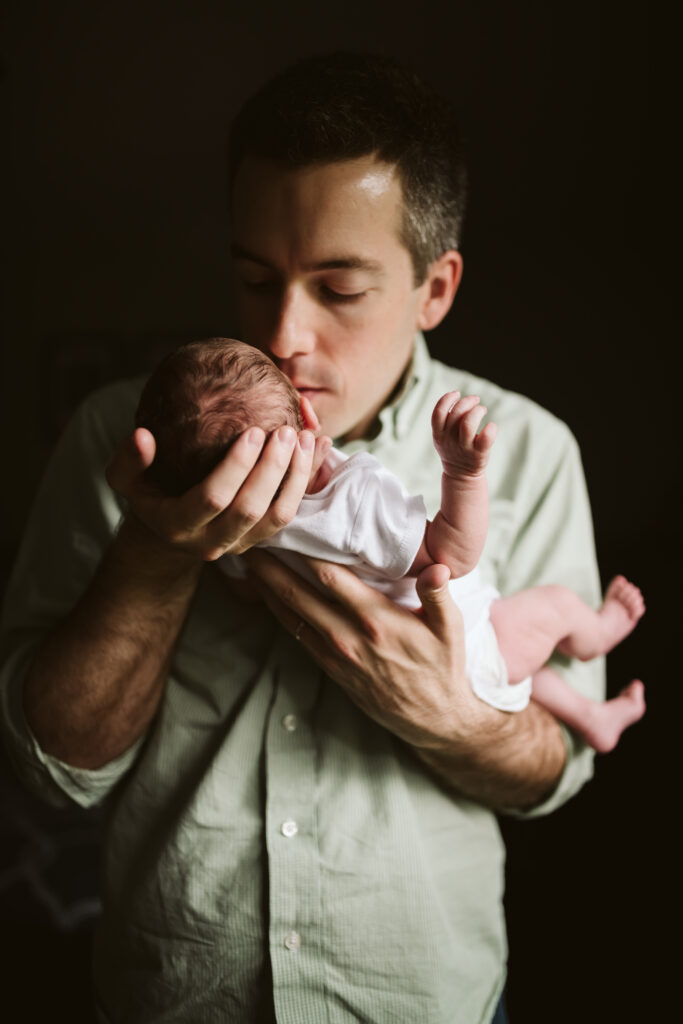 A father giving his newborn baby a kiss. Lifestyle photo by Laura Mares Photography, Pittsburgh Newborn Photographer.