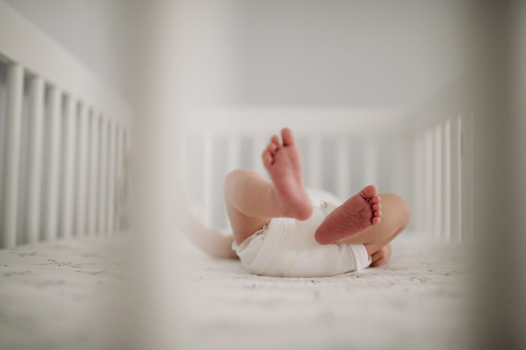 A newborn baby's feet laying in a crib. Lifestyle photo by Laura Mares Photography, Pittsburgh Newborn Photographer