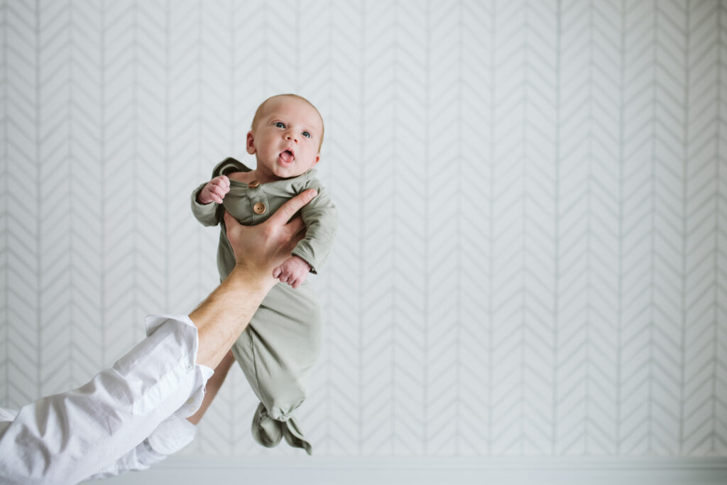 lifestyle portrait of a father's hands holding his newborn baby up