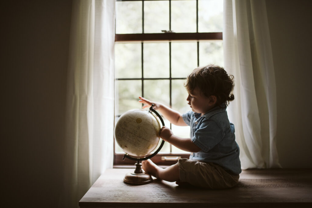 A toddler boy sitting inside a window lookin at a globe. Lifestyle photo by Laura Mares Photography, Pittsburgh Lifestyle Photographer.