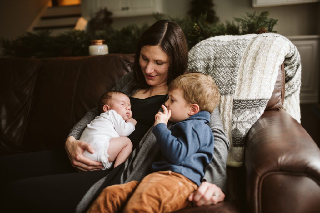 A mother holding her two babies on the sofa. Lifestyle photo by Laura Mares Photography, Pittsburgh Newborn Photographer.