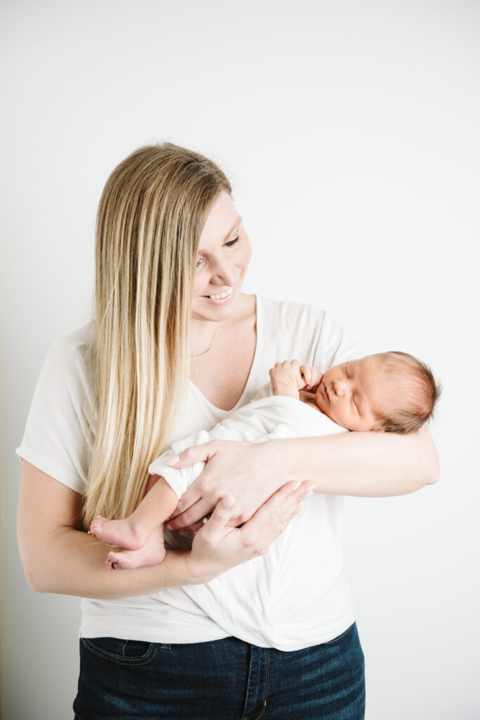 mother holding newborn baby wearing white in white studio