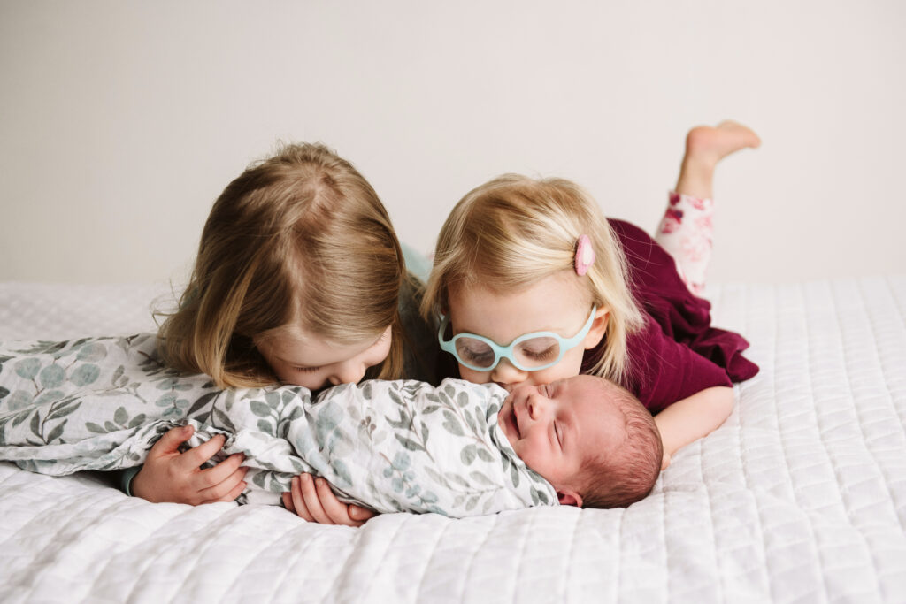 big sisters kissing happy newborn baby