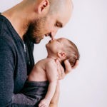 Portrait of a father holding his newborn son in his arms in the studio. Photo by Laura Mares Photography, Pittsburgh Newborn Photographer.