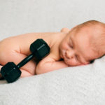 A portrait of a posed newborn with a dumbbell in studio. Photo by Laura Mares Photography, Pittsburgh Newborn Photographer.