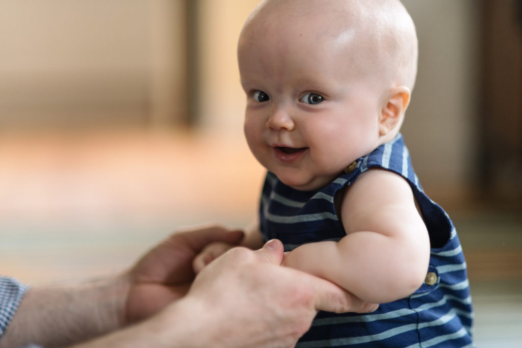 a lifestyle portrait of a baby boy smiling while holding his parents hands