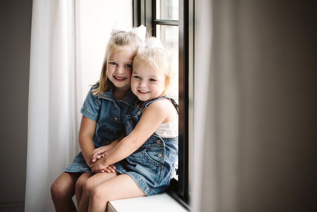 lifestyle portrait of young girls sitting on a widow sill