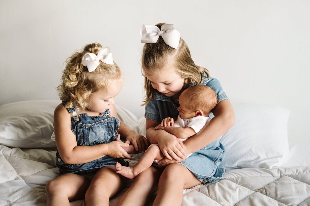 lifestyle portrait of sisters holding newborn baby