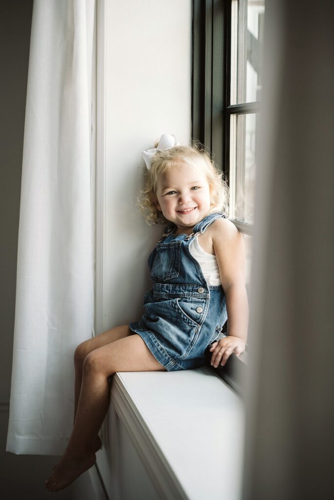 lifestyle portrait of young girl sitting on a widow sill