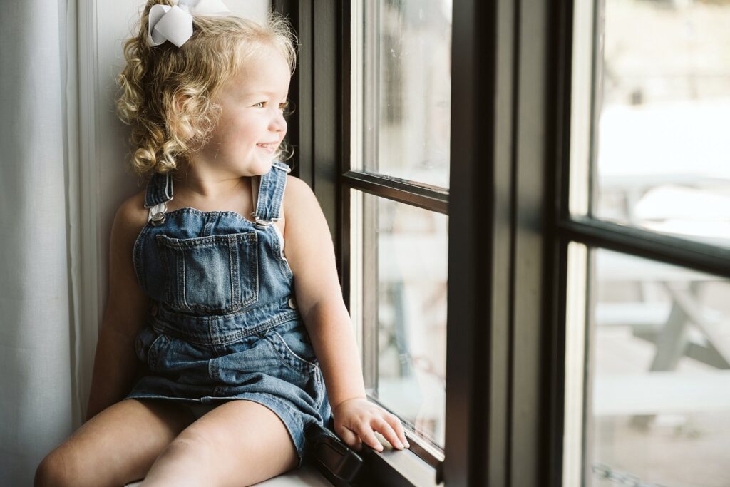 lifestyle portrait of young girl sitting on a widow sill