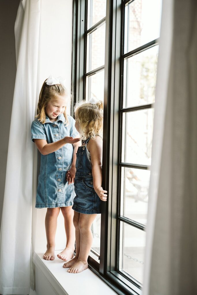 lifestyle portrait of young girls standing on a widow sill