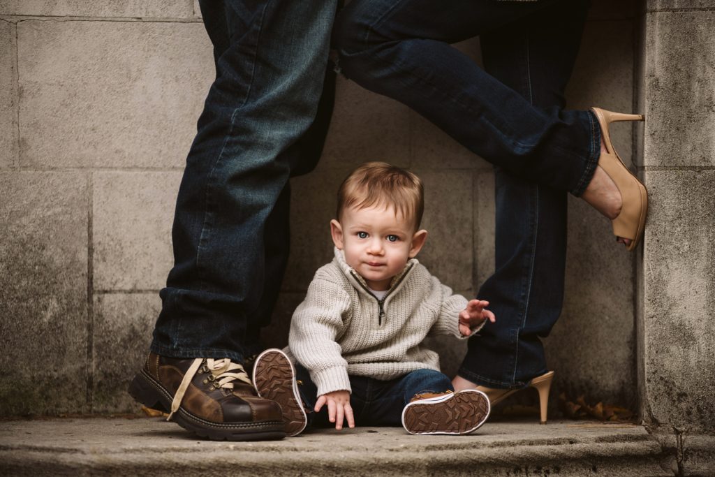 A baby sitting between his parents legs for family pictures at Mellon Park. Photo by Laura Mares Photography, Pittsburgh Family Photographer.