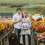 Lifestyle image of a maternity couple standing between flowers with their dog near Pittsburgh. Portrait by Laura Mares Photography, Pittsburgh Maternity Photographer