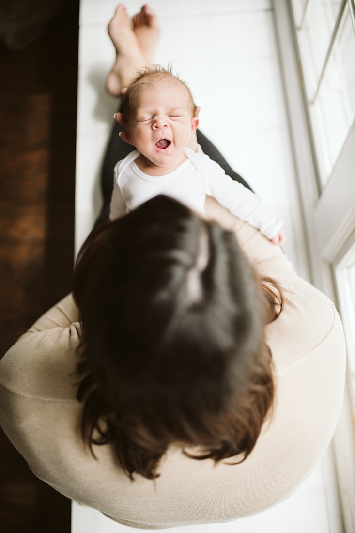 A newborn lifestyle image of a mother sitting on a window seat holding her newborn baby boy. Photo by Pittsburgh Newborn Lifestyle Photographer, Laura Mares Photography.