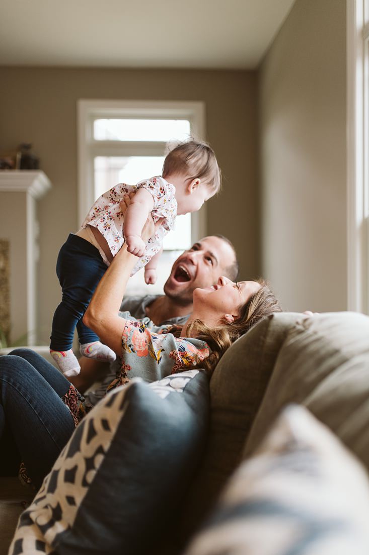 A lifestyle image of a family sitting on the sofa holding their baby girl. Photo by Pittsburgh Lifestyle Photographer, Laura Mares Photography.