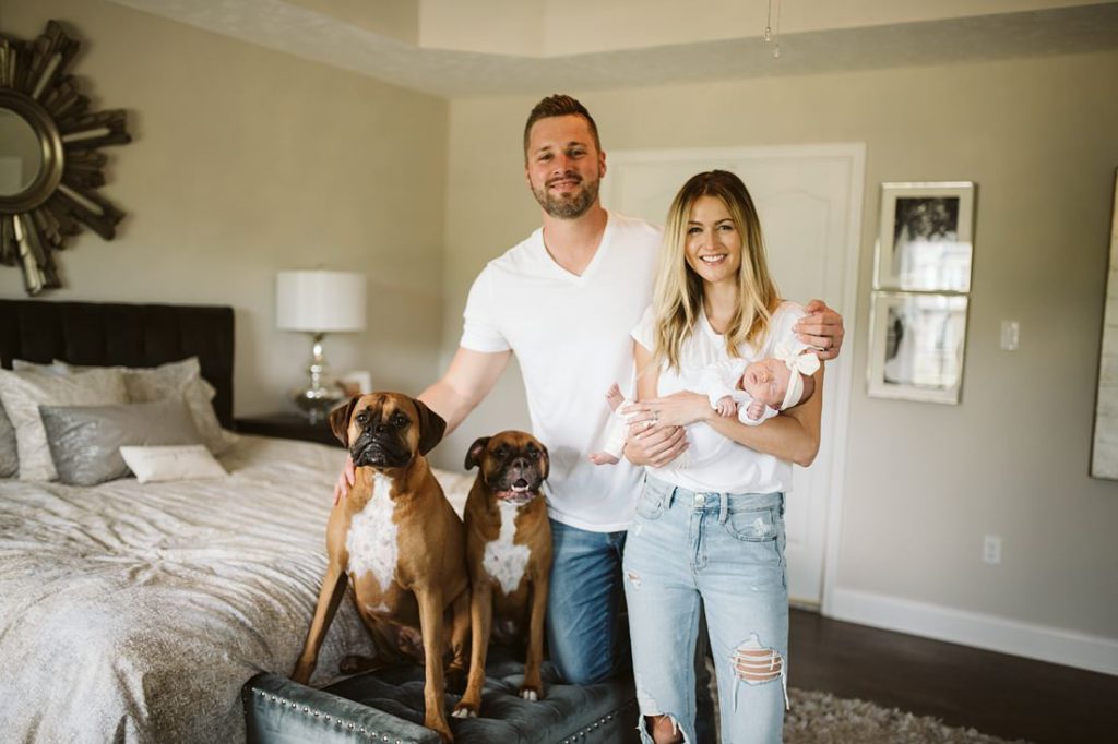 A newborn lifestyle image of a family standing in their bedroom with their newborn baby and two dogs. Photo by Pittsburgh Newborn Lifestyle Photographer, Laura Mares Photography.