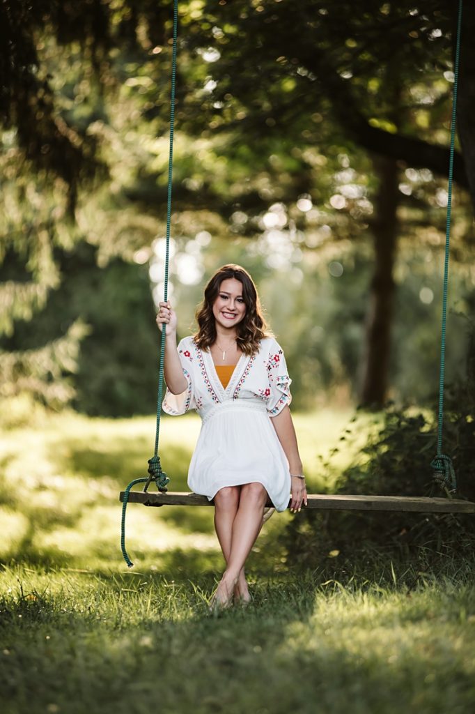 Portrait of a high school senior girl sitting on a rustic swing at sunset. Photo by Laura Mares Photography, Pittsburgh Senior Photographer.