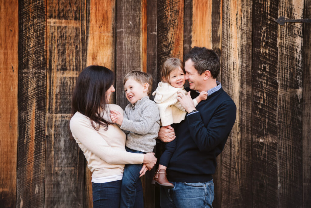 family of four hugging and laughing in front of a wooden background