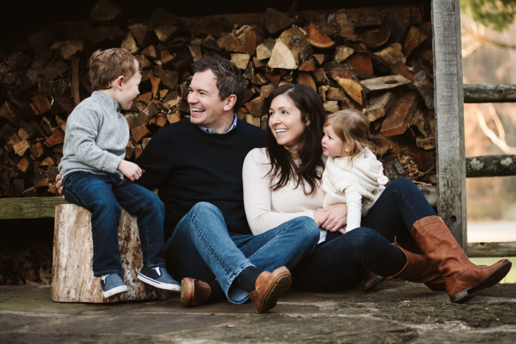 a family of four sitting together for a picture infront of a wood pile