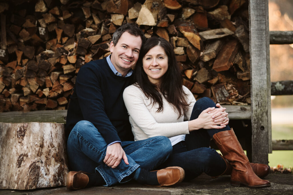 a couple sitting together for a picture infront of a wood pile