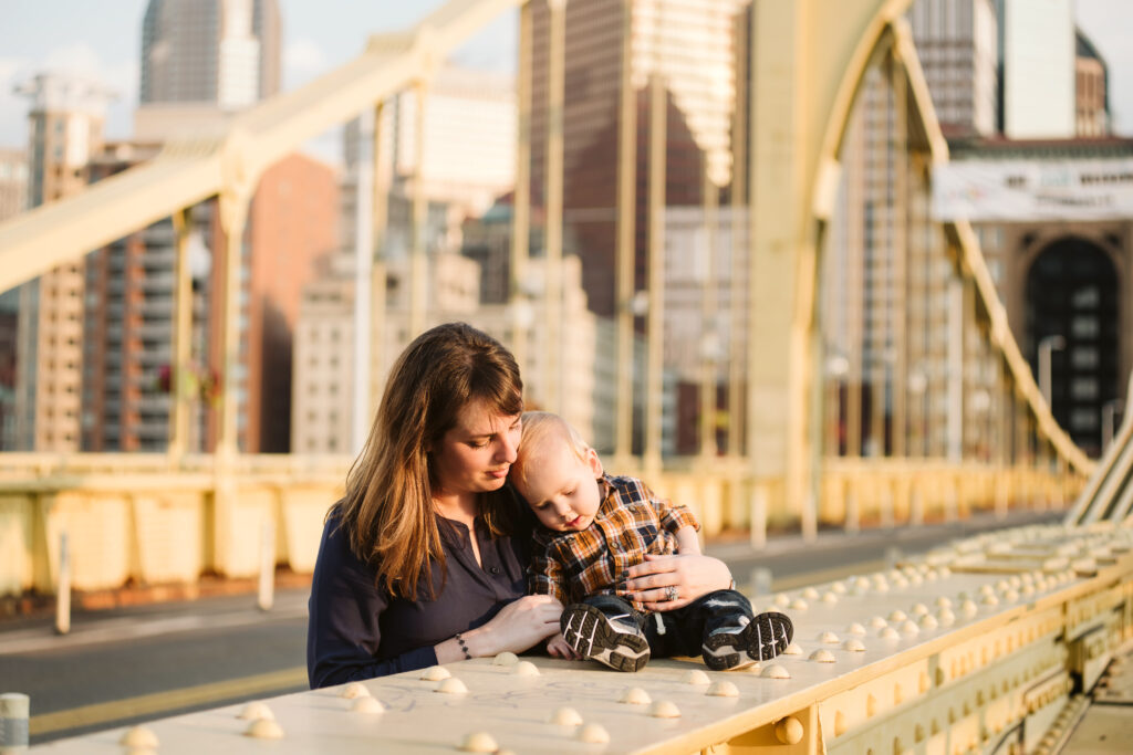 a mother and her one year old son standing on a yellow bridge at sunset