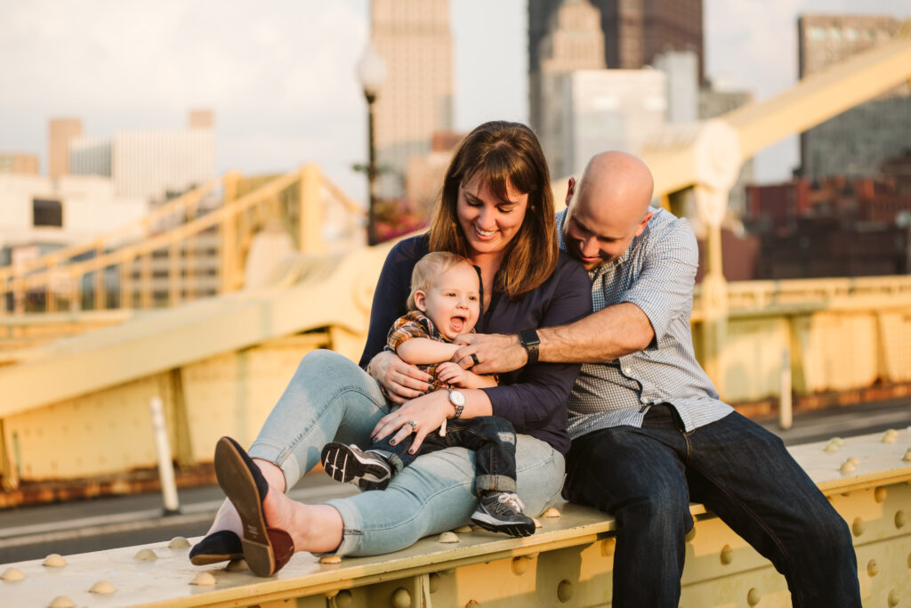 a family of three sitting on a yellow bridge at sunset