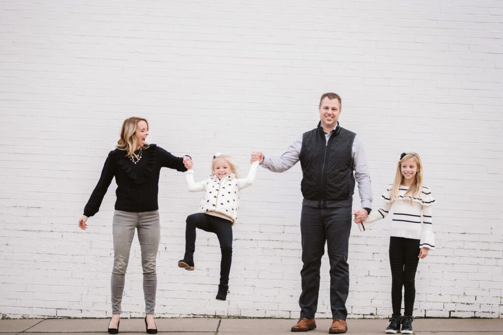 a family of four standing in front of a white brick wall