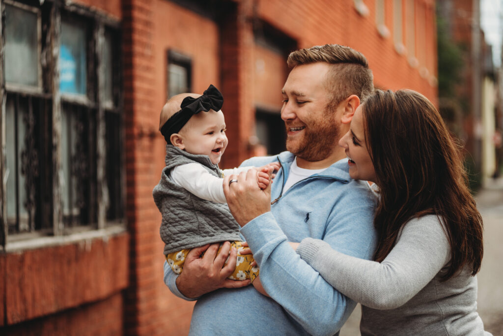 a family of three looking at each other in front of a brick wall in North Side of Pittsburgh