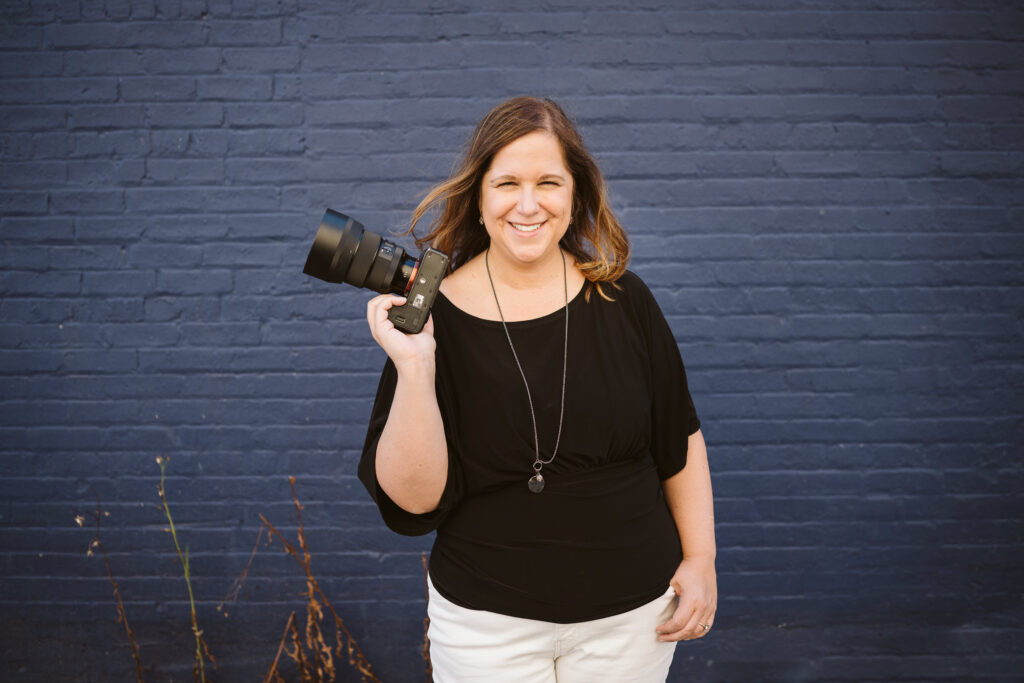 personal branding portrait of a photographer holding a camera in front of a blue brick wall