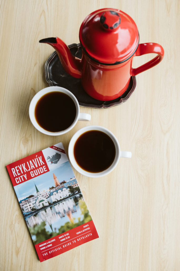 Red coffee pot, two cups of black coffee and a Reykjavik city guide.