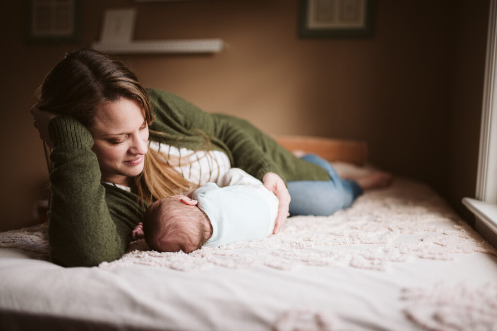 a mom and her baby girl laying on a bed near a window