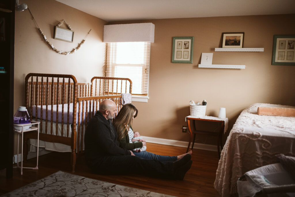 a family of three sitting in front of a crib in the nursery