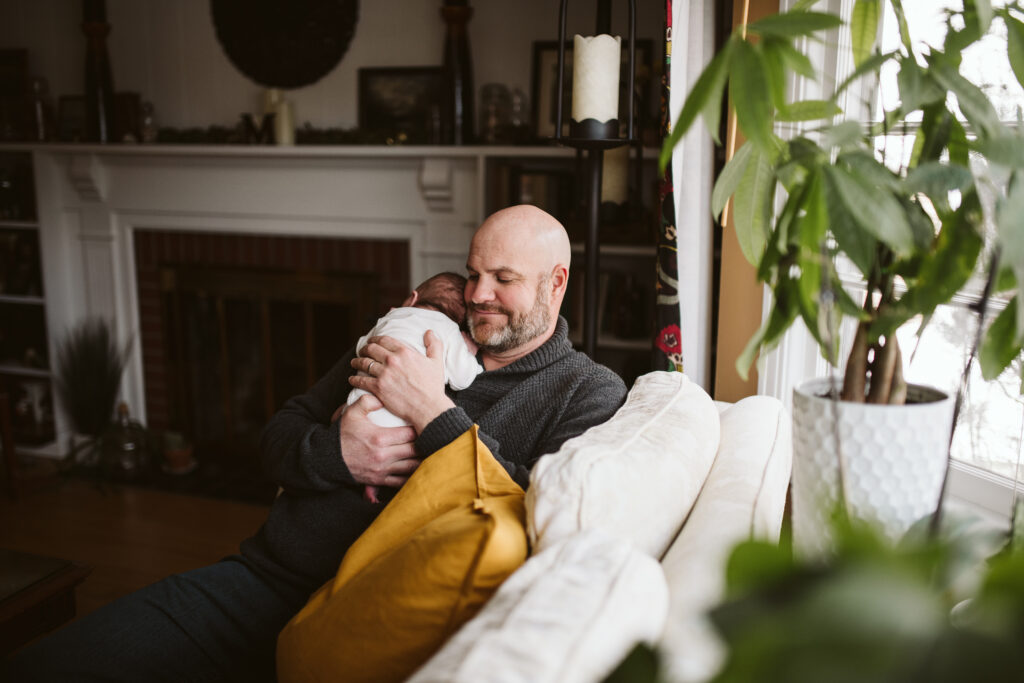 a father holding his baby girl in the living room with lots of houseplants nearby