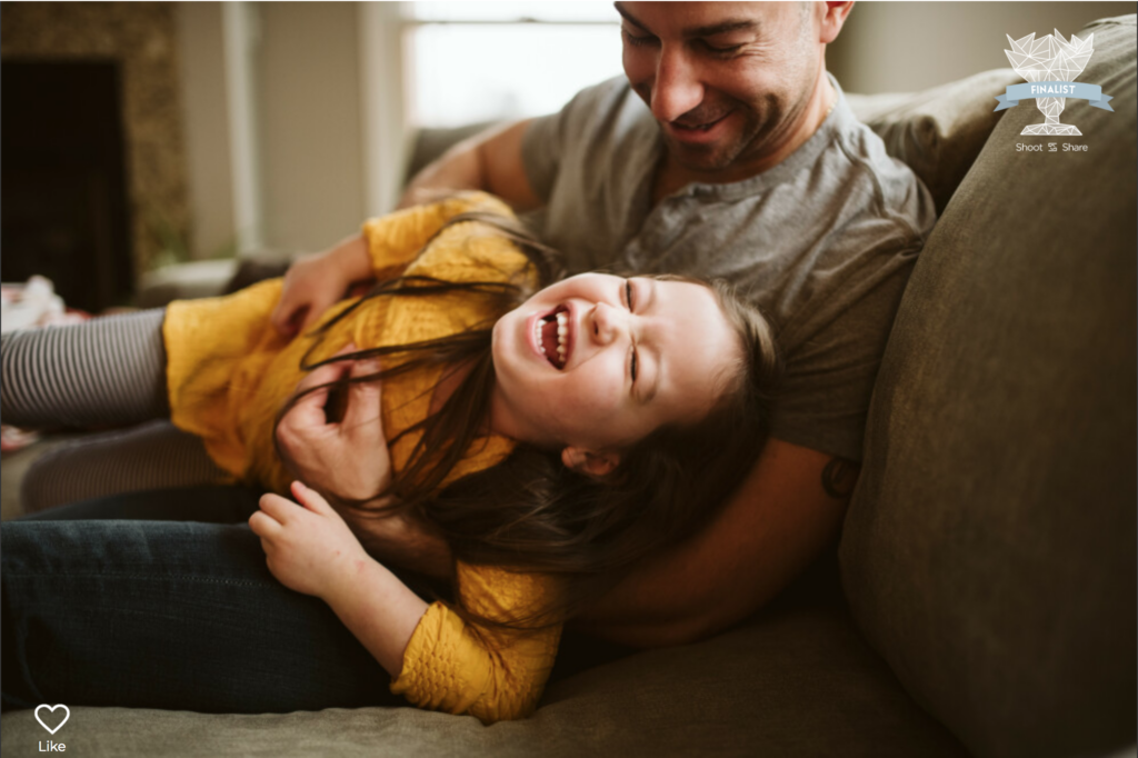 A father and daughter laughing on their sofa