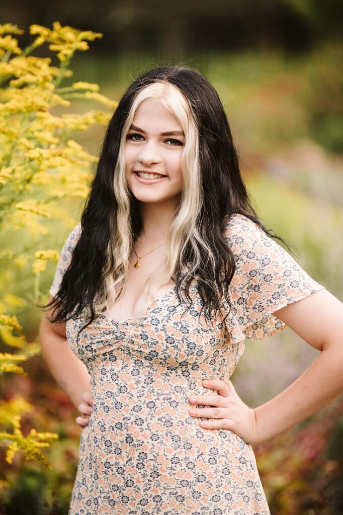 high school senior girl standing near yellow flowers during golden hour