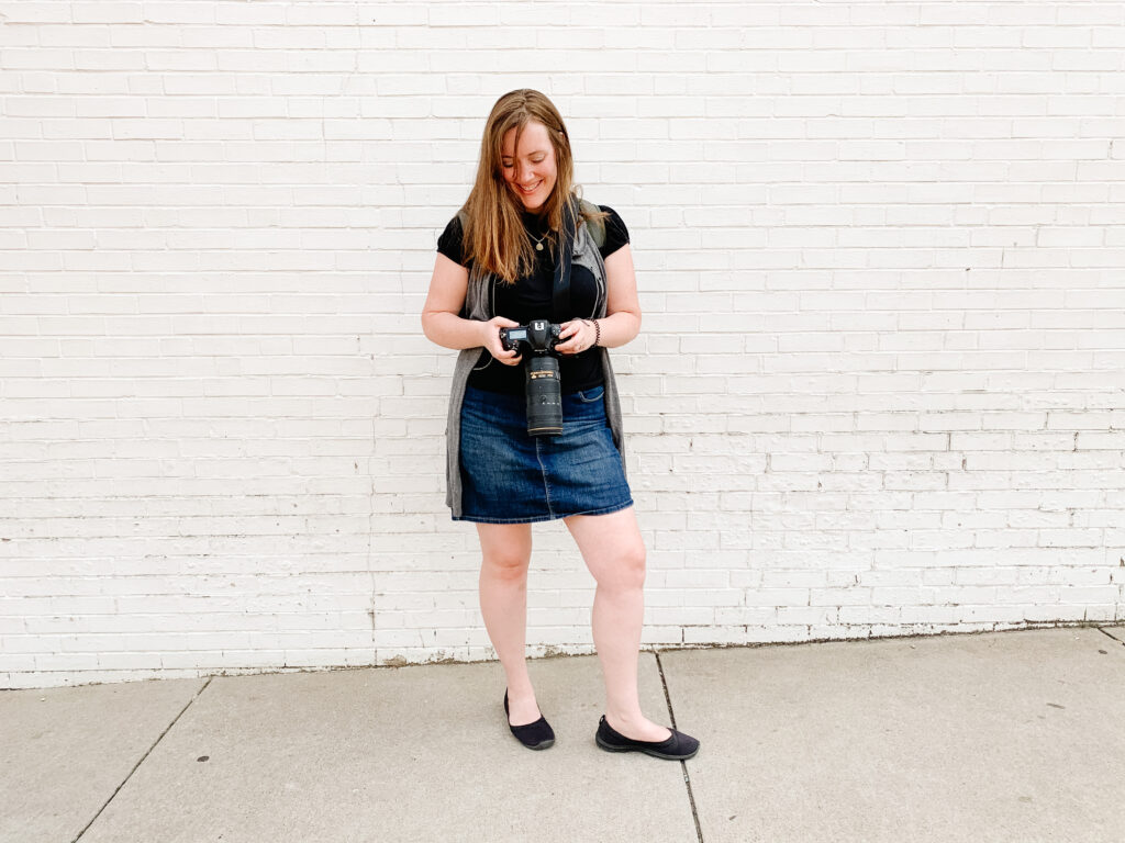 Laura Mares, Pittsburgh Photographer standing in front of a white wall holding her camera