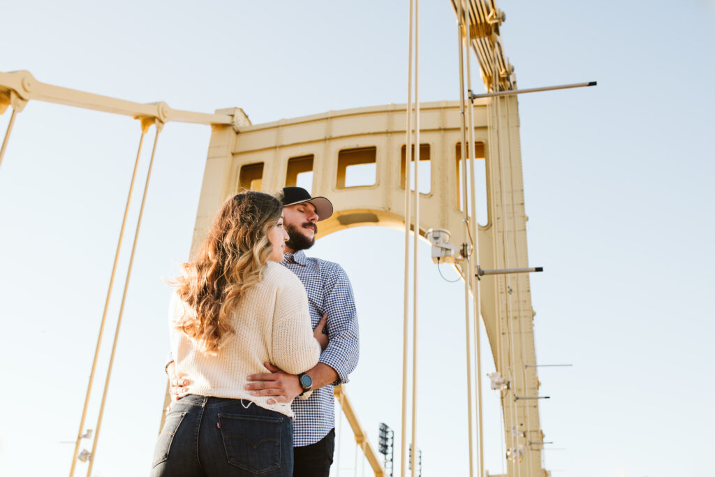 engaged couple standing on the Roberto clemente bridge at sunset in downtown Pittsburgh