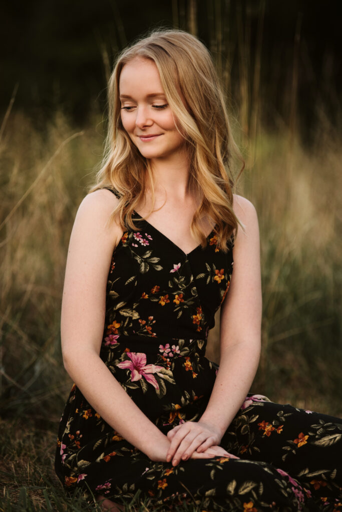 Portrait of a high school senior girl sitting in a grassy field during sunset