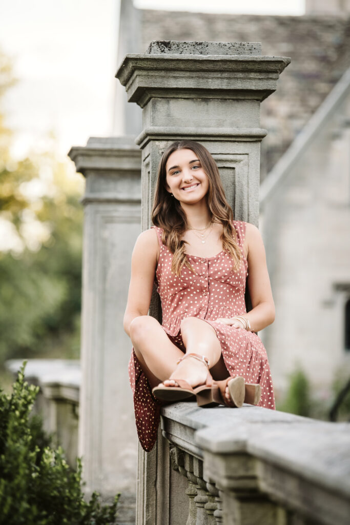 senior portrait of a girl wearing a dress leaning against a pillar at Hartwood Acres