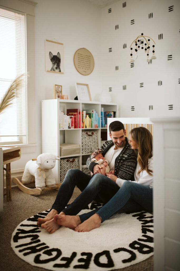 beautiful family holding newborn baby sitting near the crib in modern boho nursery