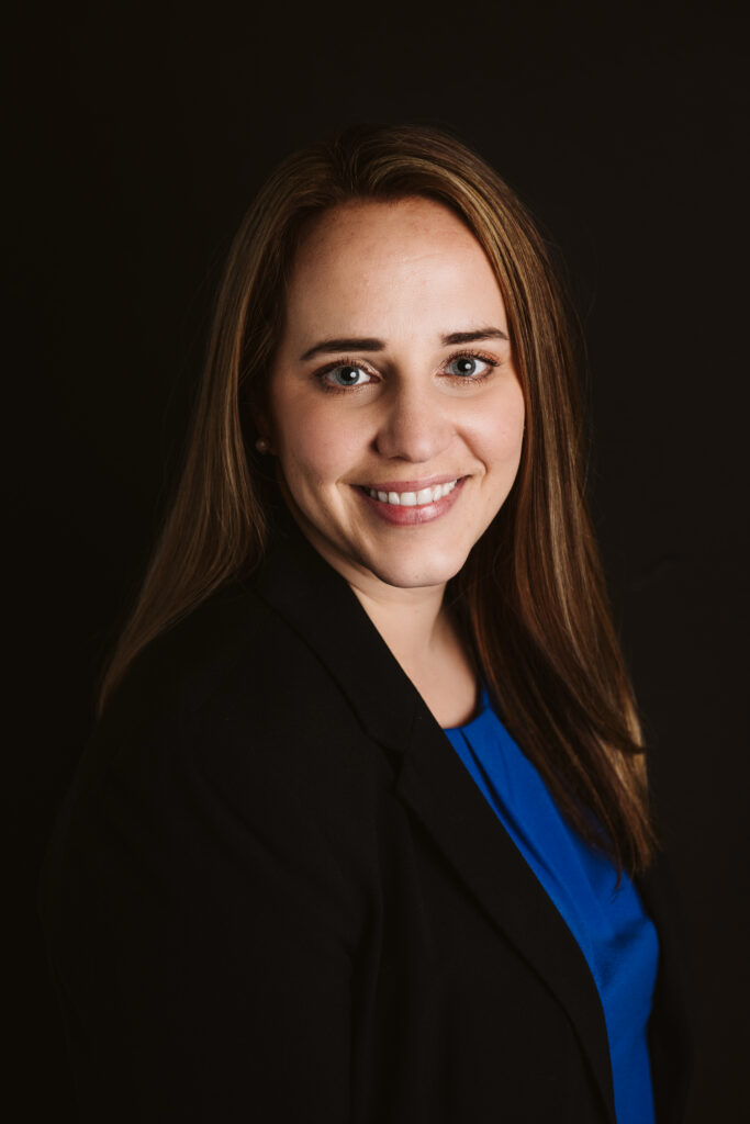 Professional headshot of a business woman wearing a black suit with a black background. Portrait taken by Laura Mares Photography, Pittsburgh Photographer.