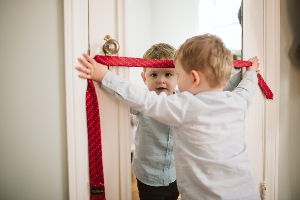 lifestyle photo of a boy holding his dad's tie while looking in the mirror