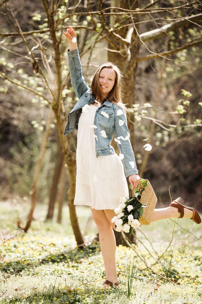 senior pictures of a girl dropping rose petals in a forest near Pittsburgh